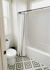 Bathroom with a wealth of natural light, tile patterned floors, toilet, and shower / bath combo with shower curtain