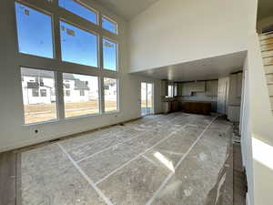 Unfurnished living room featuring a towering ceiling and baseboards