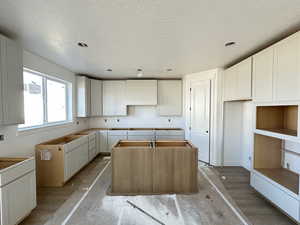 Kitchen with custom range hood, a textured ceiling, a kitchen island, and light wood-type flooring