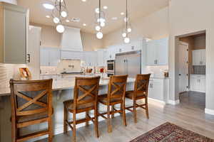 Kitchen with white cabinets, stainless steel appliances, light stone counters, and custom exhaust hood