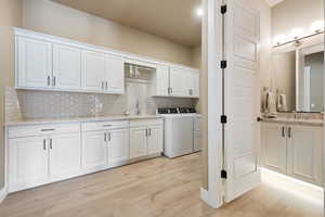 Interior space featuring washing machine and dryer, light hardwood / wood-style floors, tasteful backsplash, and white cabinets