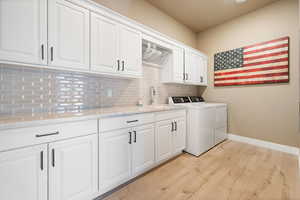 Laundry room featuring sink, separate washer and dryer, cabinets, and light hardwood / wood-style floors