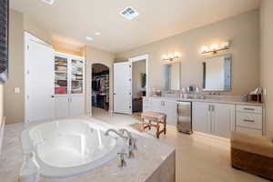 Bathroom with tile patterned flooring, vanity, and a relaxing tiled tub