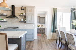 Kitchen with decorative light fixtures, wall chimney exhaust hood, tasteful backsplash, and stainless steel gas cooktop