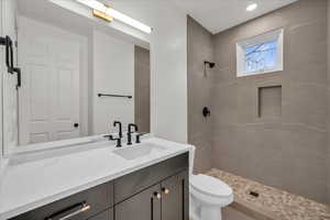 Bathroom featuring tiled shower, vanity, and toilet