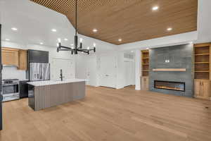 Kitchen with an island with sink, light hardwood / wood-style flooring, sink, appliances with stainless steel finishes, and pendant lighting