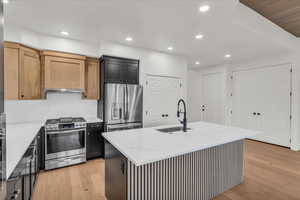 Kitchen featuring a center island with sink, stainless steel appliances, light hardwood / wood-style floors, sink, and light stone counters