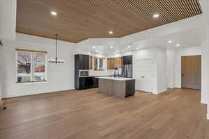 Kitchen featuring a center island with sink, appliances with stainless steel finishes, an inviting chandelier, light wood-type flooring, and wood ceiling