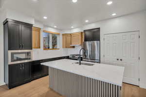 Kitchen with stainless steel appliances, light stone countertops, light brown cabinets, light wood-type flooring, and a kitchen island with sink