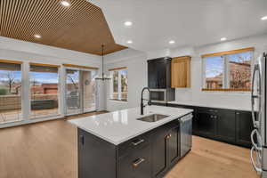 Kitchen with a center island with sink, stainless steel appliances, light hardwood / wood-style flooring, decorative light fixtures, and sink