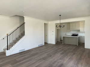 Unfurnished living room with stairway, dark wood-style floors, a notable chandelier, and visible vents