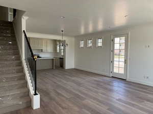Unfurnished living room with stairs, crown molding, a chandelier, and wood finished floors