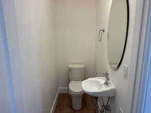 Bathroom featuring baseboards, wood finished floors, a sink, and toilet