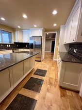 Kitchen featuring appliances with stainless steel finishes, white cabinetry, dark stone counters, and light hardwood / wood-style flooring