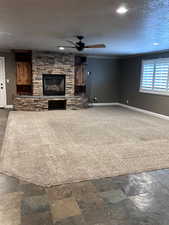 Unfurnished living room with dark carpet, a textured ceiling, ceiling fan, crown molding, and a fireplace