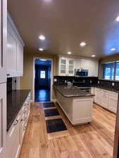 Kitchen featuring white cabinets, appliances with stainless steel finishes, dark stone counters, and light hardwood / wood-style flooring