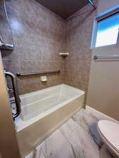 Bathroom featuring a textured ceiling, toilet, and tiled shower / bath combo