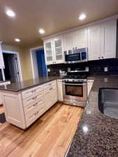 Kitchen with dark stone countertops, appliances with stainless steel finishes, white cabinets, and light hardwood / wood-style floors