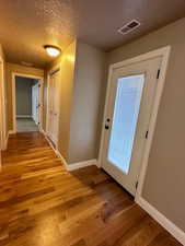 Doorway with light wood-type flooring and a textured ceiling