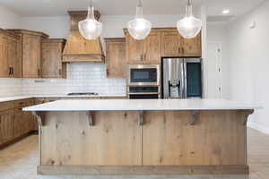 Kitchen featuring stainless steel appliances, a kitchen island, custom range hood, a kitchen breakfast bar, and decorative backsplash