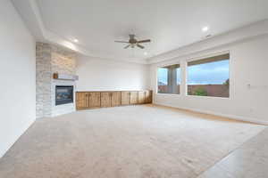 Unfurnished living room with a fireplace, ceiling fan, light carpet, and a tray ceiling