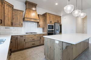 Kitchen with a breakfast bar, premium range hood, stainless steel appliances, hanging light fixtures, and tasteful backsplash