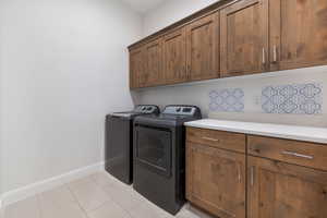 Washroom featuring washing machine and clothes dryer, light tile patterned flooring, and cabinets