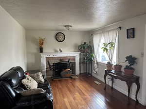 Living room with wood finished floors, visible vents, baseboards, a textured ceiling, and a fireplace