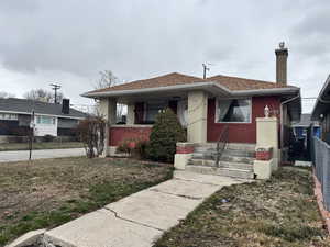 Bungalow-style house featuring fence, a chimney, a shingled roof, and brick siding