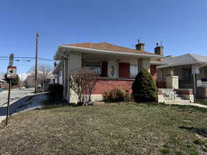 Bungalow-style home featuring brick siding, a chimney, a front yard, and a shingled roof