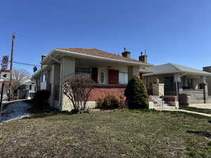 View of front facade with brick siding, a chimney, roof with shingles, fence, and a front yard