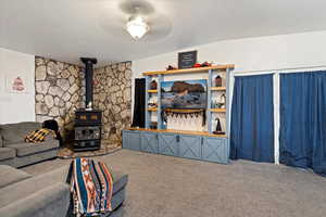 Carpeted living room featuring a wood stove, ceiling fan, and a textured ceiling