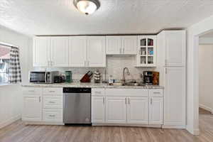 Kitchen featuring stainless steel appliances, light stone counters, light hardwood / wood-style floors, sink, and white cabinetry