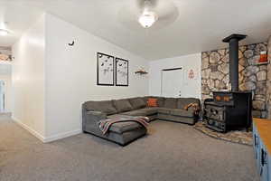 Carpeted living room featuring ceiling fan, a wood stove, and a textured ceiling