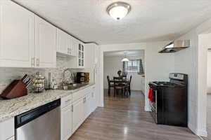 Kitchen with light wood-type flooring, stainless steel appliances, sink, light stone counters, and white cabinets