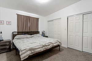 Carpeted bedroom with a textured ceiling, lofted ceiling, and two closets