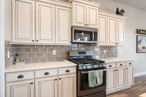 Kitchen featuring appliances with stainless steel finishes, light stone counters, dark hardwood / wood-style floors, cream cabinets, and tasteful backsplash