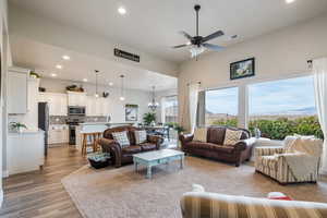 Living room with light wood-type flooring and ceiling fan with notable chandelier