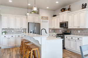 Kitchen with white cabinets, appliances with stainless steel finishes, sink, and a kitchen island with sink