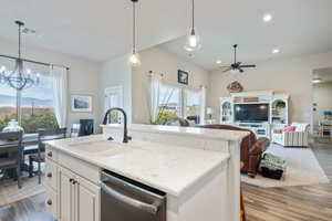 Kitchen with hanging light fixtures, light stone countertops, stainless steel dishwasher, sink, and a kitchen island with sink