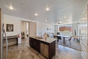 Kitchen featuring a center island with sink, sink, dark brown cabinets, a textured ceiling, and appliances with stainless steel finishes