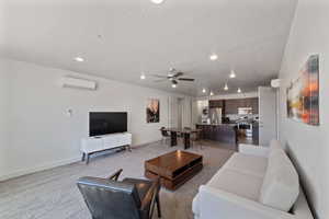 Carpeted living room featuring ceiling fan, an AC wall unit, and a textured ceiling