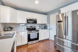 Kitchen with white cabinetry, sink, tasteful backsplash, dark wood-type flooring, and appliances with stainless steel finishes