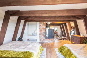 Bedroom featuring beamed ceiling, wood-type flooring, and wood walls