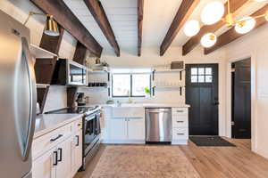 Kitchen with white cabinetry, tasteful backsplash, decorative light fixtures, appliances with stainless steel finishes, and beamed ceiling