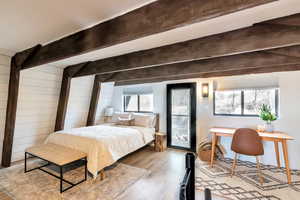 Bedroom featuring beamed ceiling, wooden walls, light hardwood / wood-style floors, and access to exterior