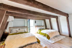 Bedroom with beamed ceiling, wooden walls, a wall mounted AC, and light hardwood / wood-style floors