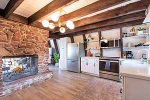 Kitchen with pendant lighting, white cabinetry, backsplash, stainless steel appliances, and light hardwood / wood-style floors