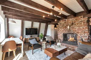 Living room with wooden walls, a stone fireplace, beam ceiling, and light wood-type flooring