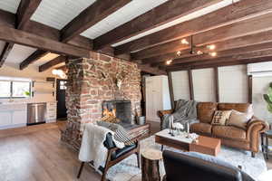 Living room featuring a stone fireplace, sink, light hardwood / wood-style flooring, a wall unit AC, and beamed ceiling